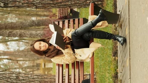 Young attractive female sitting on a bench in park alone reading a book