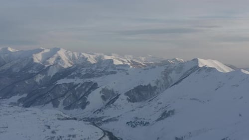 Aerial view of snow covered Caucasus mountain range and valley at sunset, pan left
