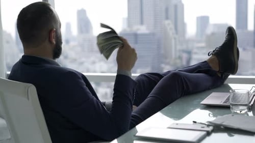 Successful, Happy Businessman Holding And Waving Money Sitting By Desk In Office