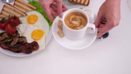 Woman Puts Cup of Fresh Espresso Coffee on a Table with Tasty Breakfast