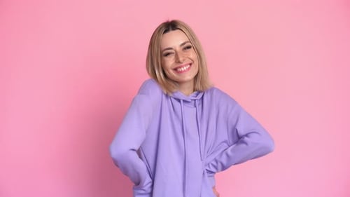 Smiling Woman in Hoodie Poses on Pink Background