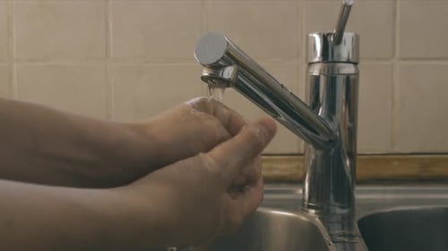 Person Washing Hands Under Faucet in the Bathroom