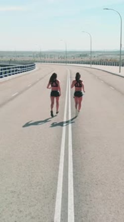 twin sisters training run on a road bridge without traffic, rear aerial view from a drone