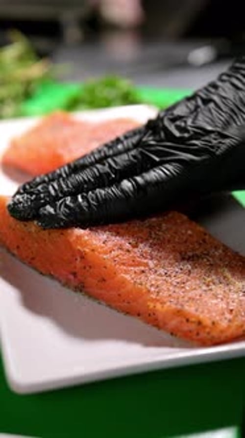 Chef preparing salmon fillets with seasoning.