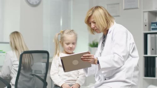 Ärztin in ihrem Büro zeigt einer kleinen Patientin einen Tablet-Computer.