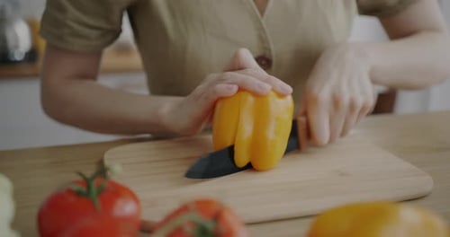 Woman Slices Yellow Pepper on Cutting Board