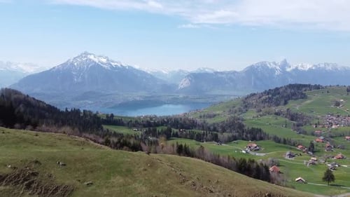 Drone flight through a green valley towards a deep blue mountain lake with the Swiss alps in the bac