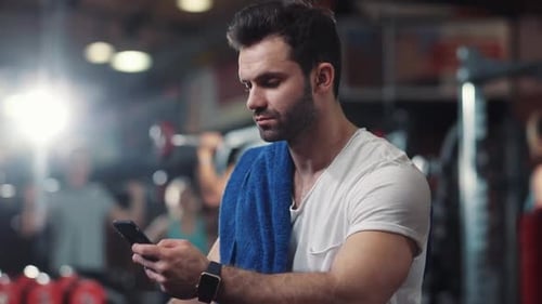 Portrait of Guy in Gym While Resting Between a Workout Uses Phone Body Strength Fit Health Male