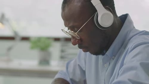 Black Office Worker In Headphones Using Laptop at Desk