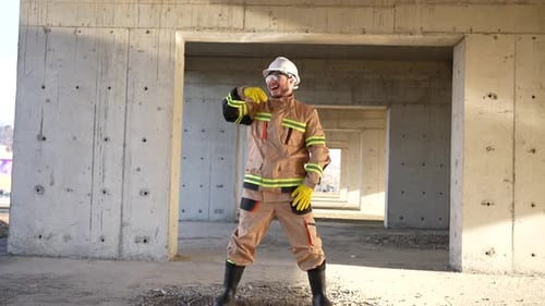Cheerful Positive Male Builder in a White Hard Hat and Uniform is Dancing on the Background of