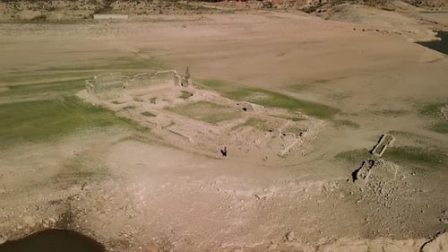 Drone shot pulling away from a tourist strolling through drought-exposed ruins adjacent to a vast la