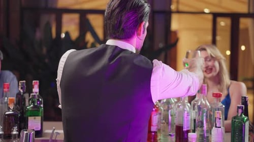 Caucasian profession bartender making a cocktail for women at a bar.