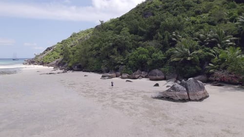Drone footage of cap ternay beach, single woman walking towards the granite rocks and taking photos