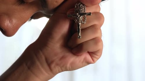 Man Holds Silver Christian Cross Pendant in Hand