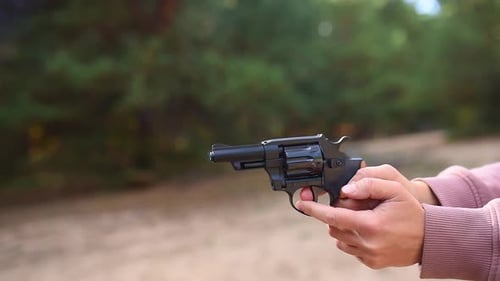 Hand Holding Black Revolver Shooting in Wooded Area
