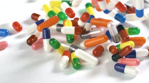 Pills fall onto a white surface in slow motion