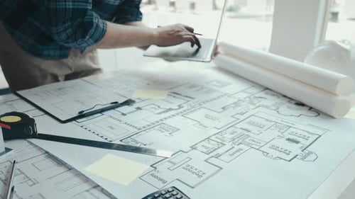 Architect Working on Blueprints with Laptop and Pencil