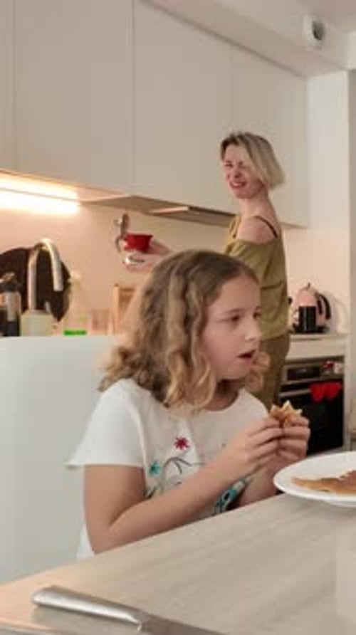 Girl Eating Breakfast While Mother Prepares Coffee