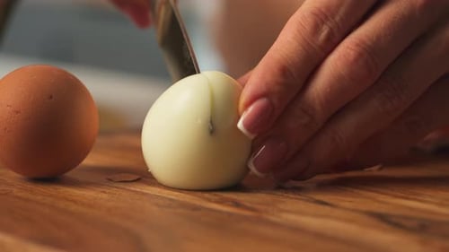 Slicing Peeled Hard-boiled Egg Into Halves On A Wooden Board. close-up shot