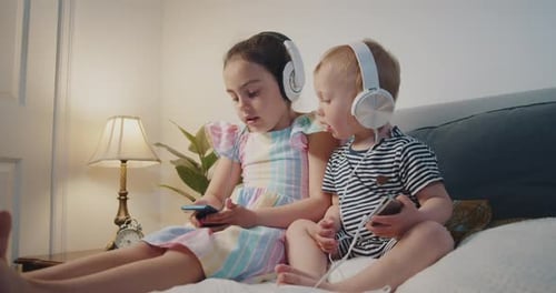 Siblings Wearing Headphones Using Phones on Bed