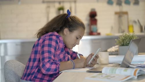 Teen Girl Studying at Table with Phone and Laptop