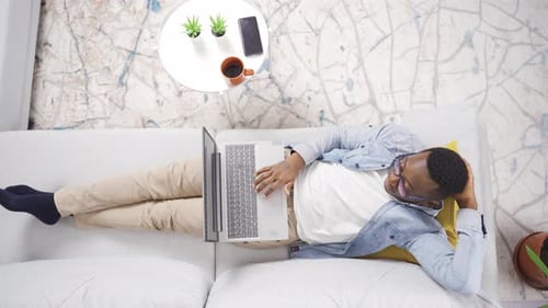 Young Man Using Laptop while Resting on Sofa