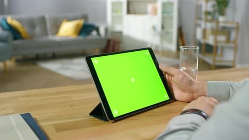 Man Holding and Watching Green Mock-up Screen Digital Tablet Computer While Sitting at the Desk. Ma