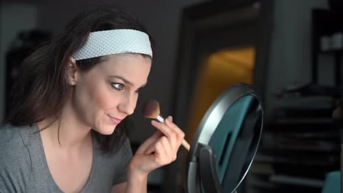 Woman Applies Makeup with Brush Looking in Mirror