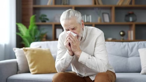 Senior Man Blowing Nose With Tissue Indoors