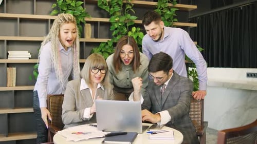 Team Celebrates Success Around Laptop in Modern Office