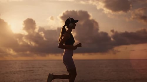 A Young Sporty Woman Runner is Listening to Music in Earphones and Training Workout Slim Fitness