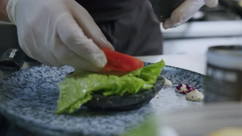 Gloved person prepares a dark bun sandwich