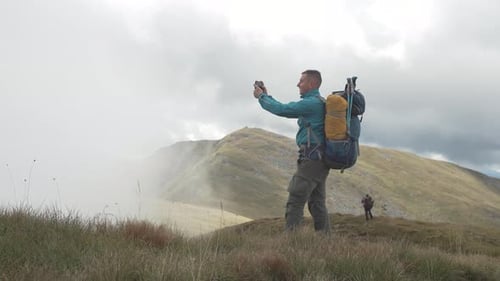 A Tourist Takes a Photo on a Phone in a Mountain Landscape