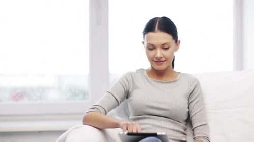 Woman Uses Tablet Device Sitting on Couch Indoors