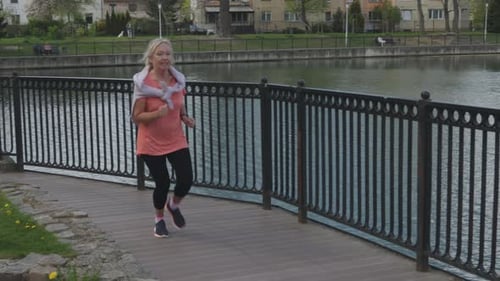 Senior Retiree Female Jogging Outdoors Sunny Daytime City Park Along Lake Road