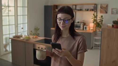 Woman Uses Phone in Modern Kitchen with Coffee