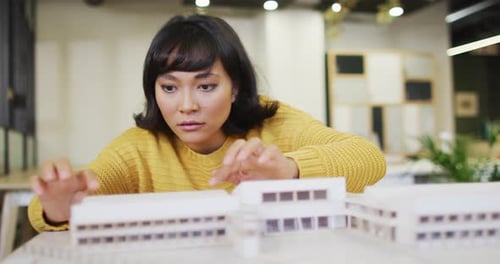 Biracial businesswoman sitting at table and working with model at office