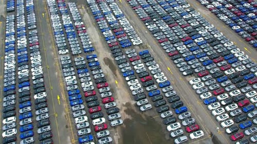 Drones flying above factory parking lot, new cars unsold