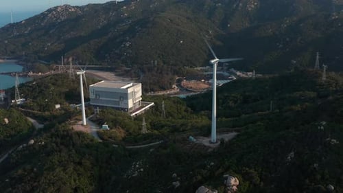 Dos generadores de turbinas eólicas y una central eléctrica en la cima de una colina junto al mar al atardecer de la hora dorada.