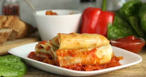 Woman adding tomato sauce onto yummy stuffed cabbage rolls at wooden table, closeup
