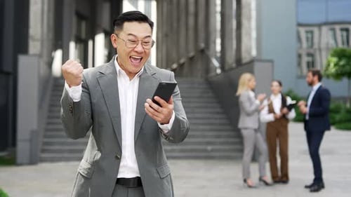Excited Businessman Celebrates with Smartphone Outside Office