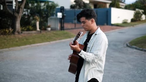 Slow Motion Shot Of An Young Male Walking In The Street While Playing An Acoustic Guitar
