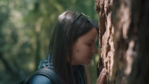 Close up of a young woman leaning on a tree trunk with her forehead