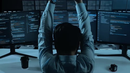 Rückansicht eines müden asiatischen Mannes, der sich beim Schreiben von Code mit mehreren Computerbildschirmen im Büro dehnt