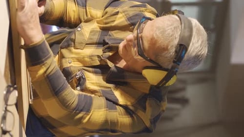 Vertical Video of Adult carpenter man working in carpentry workshop measures wood with meter.