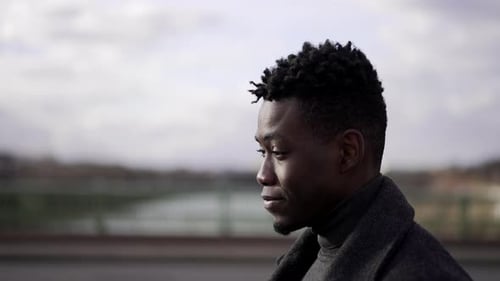 Thoughtful profile black man portrait walking outdoors in city wearing coat