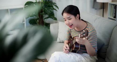 Woman plays Ukulele on Couch Indoors