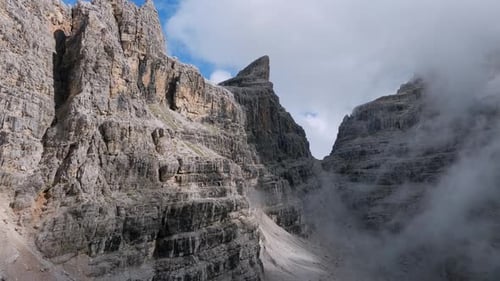Drone forward flight along rocky mountains with hovering clouds in sunlight