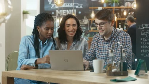 Three Young People in the Coffee Shop, They Work on a Laptop and Talk. In the Background Stylish Ca