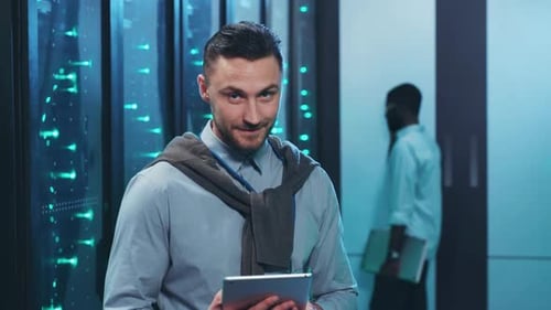 Ein Mann steht in einem Serverraum und hält ein Tablet-Gerät in der Hand